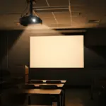 Un projecteur au plafond illumine un écran blanc dans une salle de classe sombre avec des tables et chaises