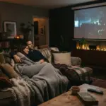 A cozy living room bathed in low, warm cinematic light at night, with a large movie screen subtly glowing